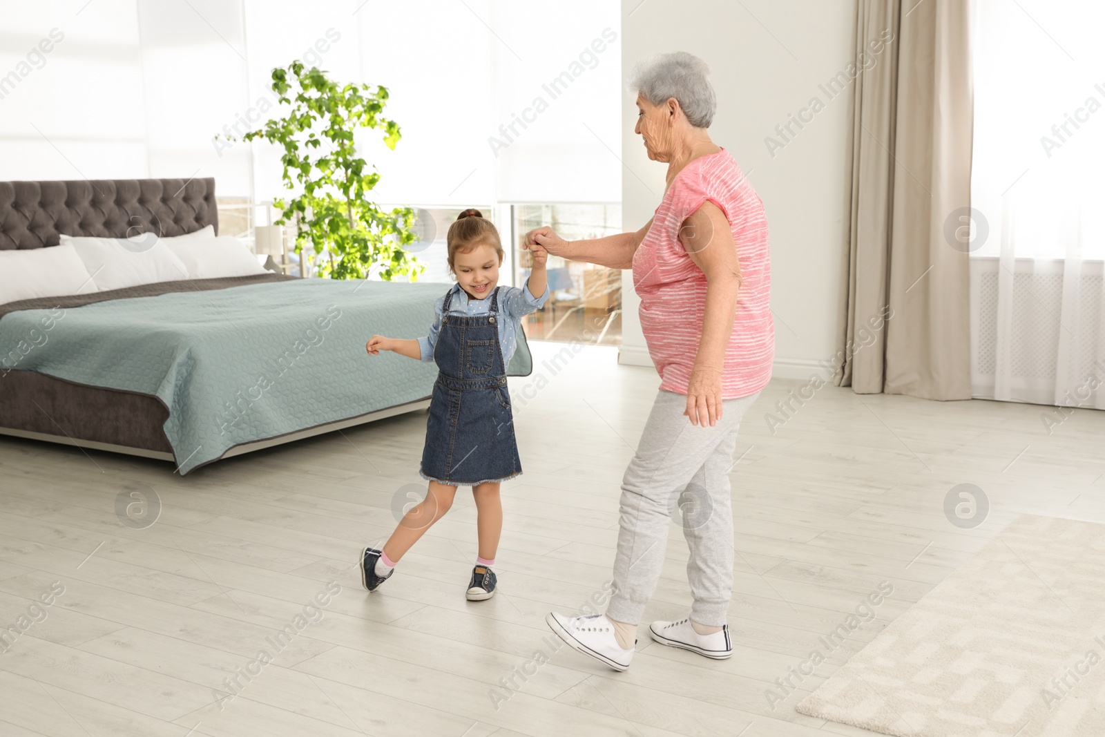 Photo of Cute girl and her grandmother dancing at home