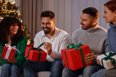 Photo of Christmas celebration in circle of friends. Happy man opening gift at home