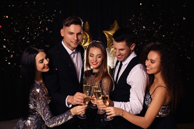Photo of Happy friends with glasses of sparkling wine celebrating New Year on black background