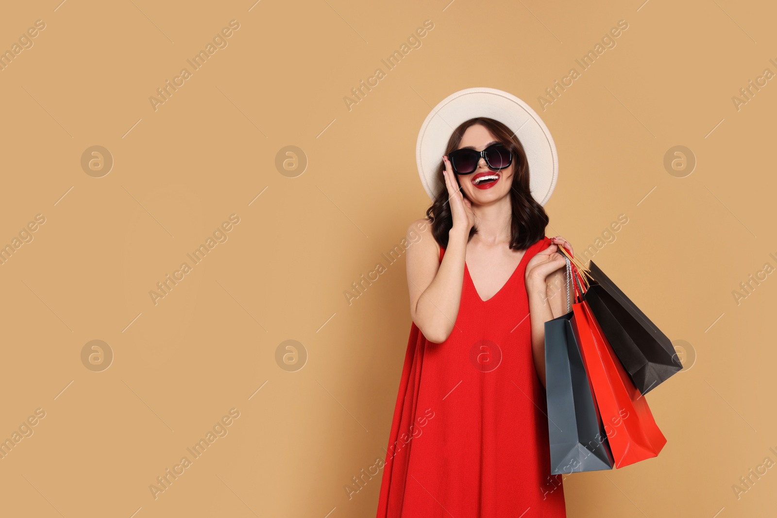 Photo of Beautiful young woman with paper shopping bags on beige background. Space for text