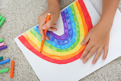 Photo of Little child drawing rainbow on floor indoors, closeup. Stay at home concept