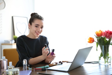 Young blogger with laptop and different cosmetics at table