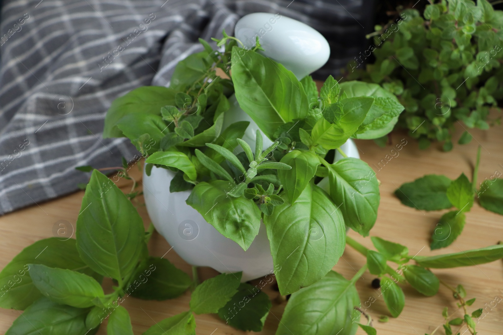 Photo of Mortar with different fresh herbs and black peppercorns on wooden table, closeup