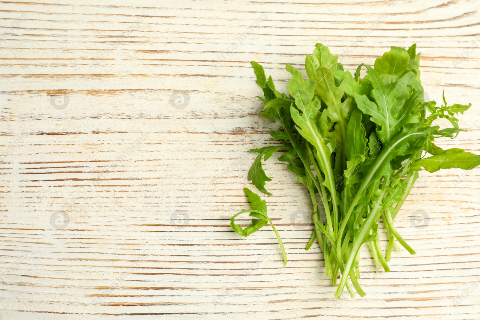 Photo of Fresh arugula on white wooden table, flat lay. Space for text