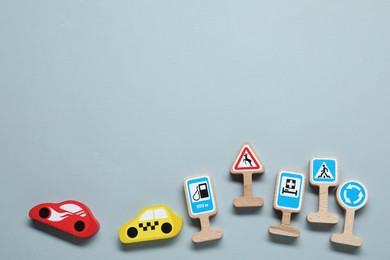 Photo of Set of wooden road signs and cars on light grey background, flat lay with space for text. Children's toy