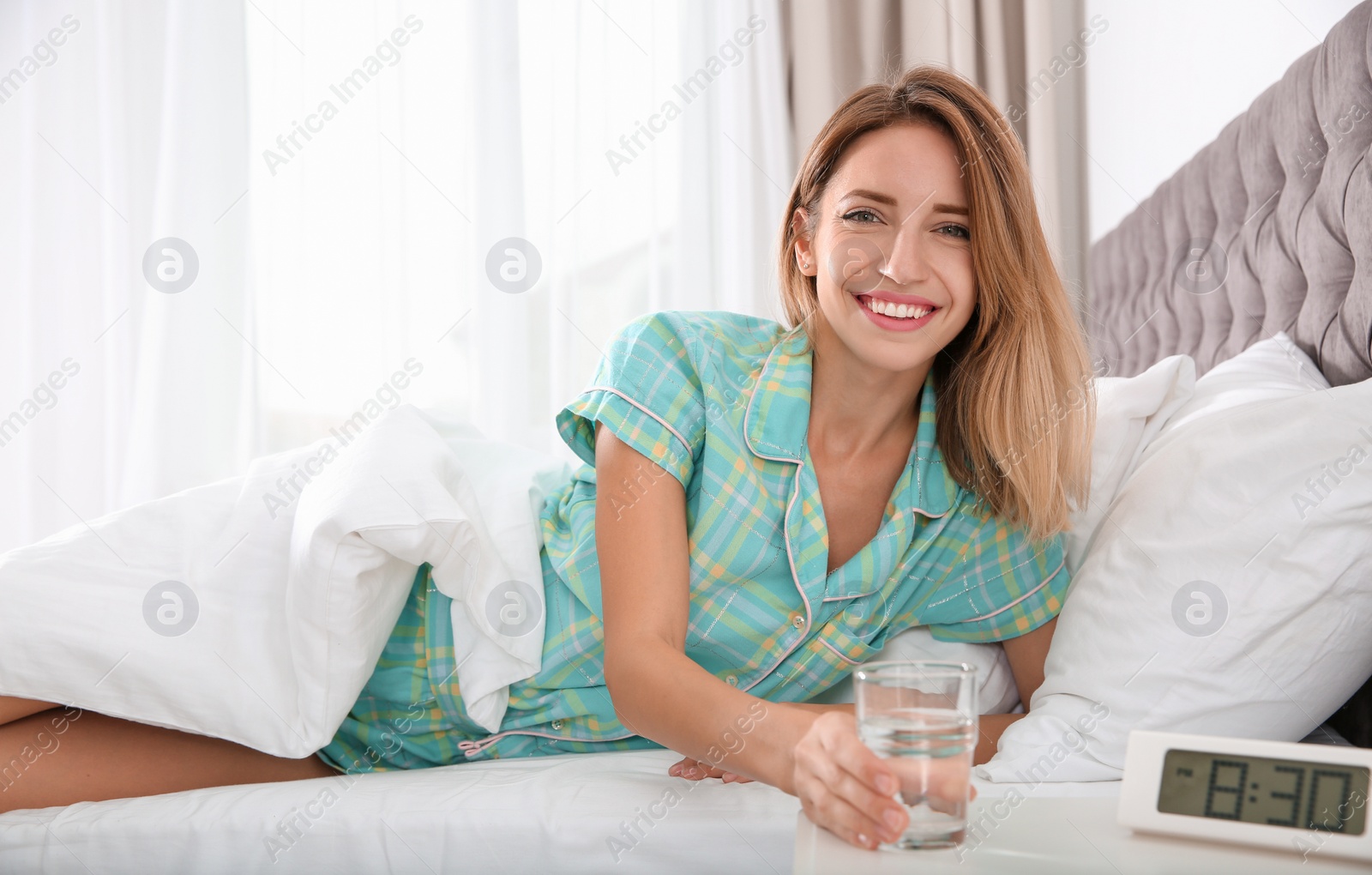 Photo of Young woman with glass of clean water lying in bed at home