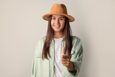 Smiling young woman showing thumb up gesture in stylish outfit on light background