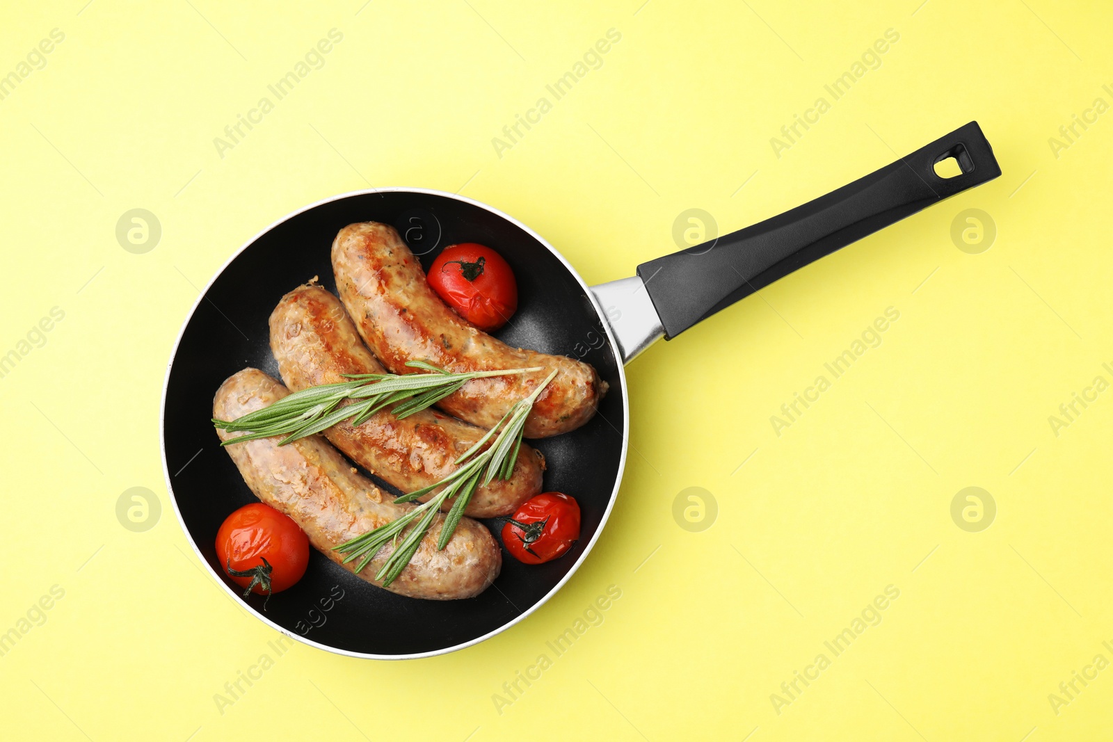 Photo of Frying pan with tasty homemade sausages, rosemary and tomatoes on yellow table, top view