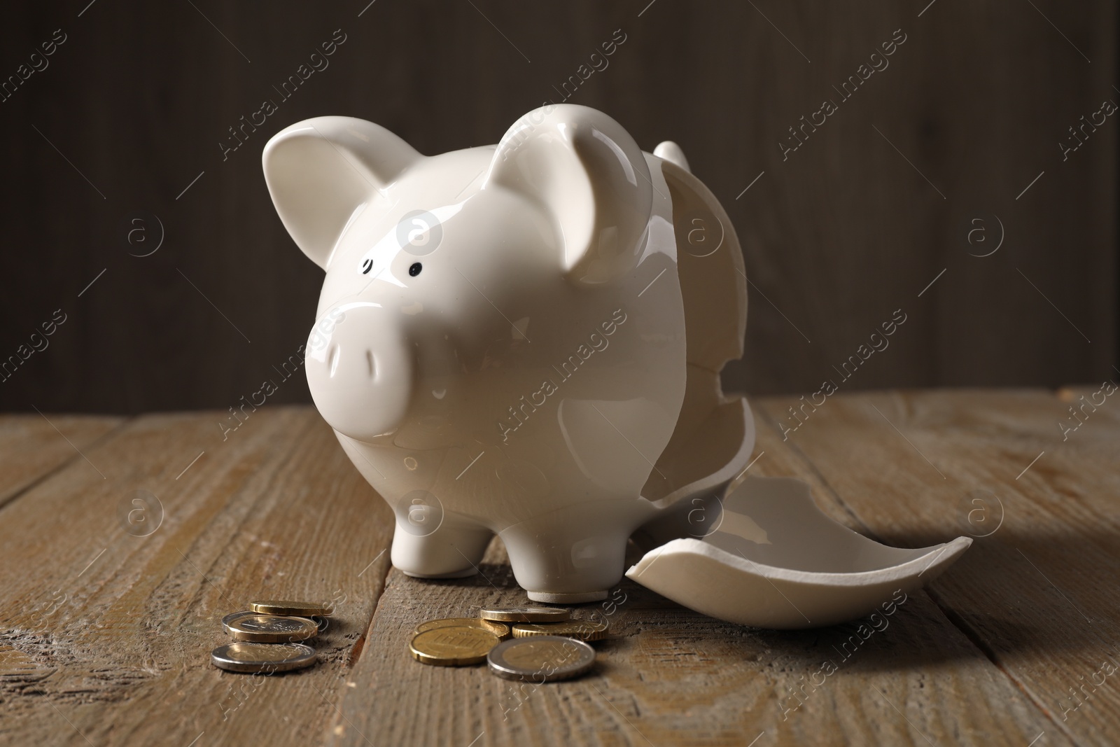 Photo of Poverty. Broken piggy bank and coins on wooden table