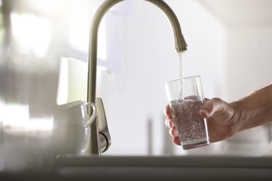 Man pouring water into glass in kitchen, closeup