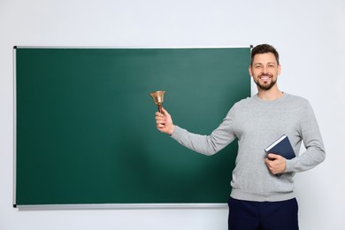 Photo of Teacher with school bell near chalkboard indoors. Space for text