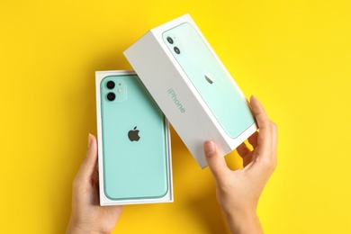 MYKOLAIV, UKRAINE - JULY 10, 2020: Woman opening box with new modern Iphone 11 Green on yellow background, top view