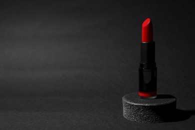 Photo of Beautiful glossy red lipstick on black background, space for text
