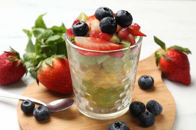 Photo of Healthy breakfast. Delicious fruit salad in glass and ingredients on white table, closeup