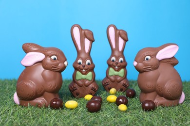 Photo of Easter celebration. Cute chocolate bunnies and tasty sweets on grass against light blue background
