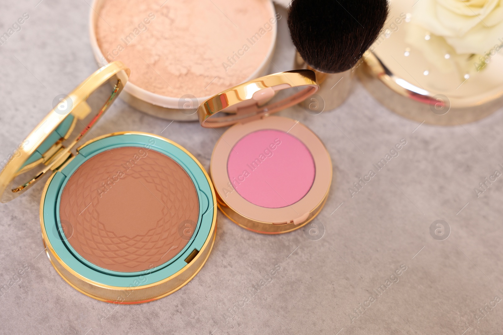 Photo of Bronzer, powder, blusher, brush and rose flower on grey textured table, above view