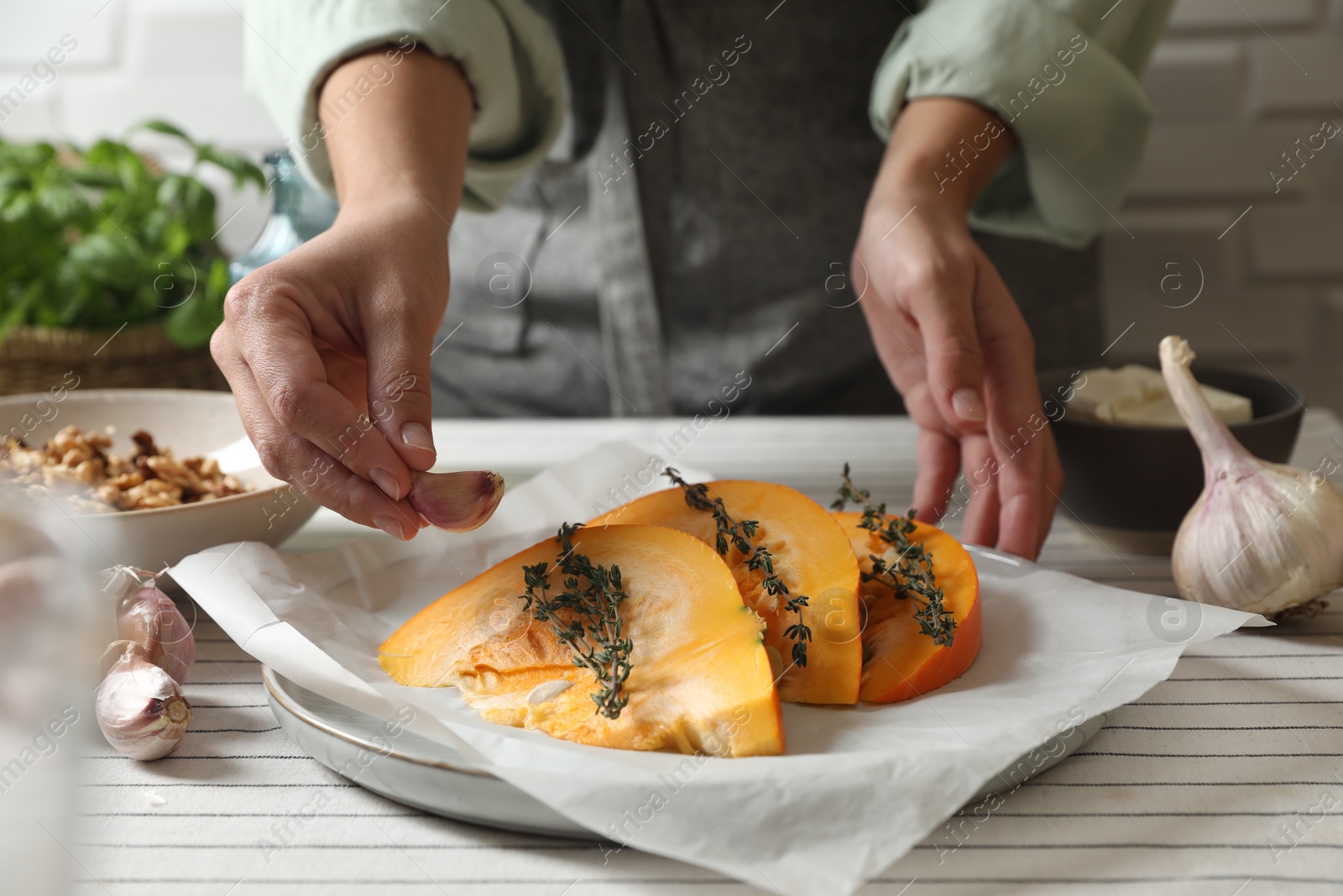 Photo of Woman putting garlic into dish with fresh ripe pumpkin slices at table, closeup