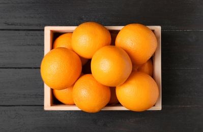 Photo of Wooden crate full of fresh oranges on dark background, top view