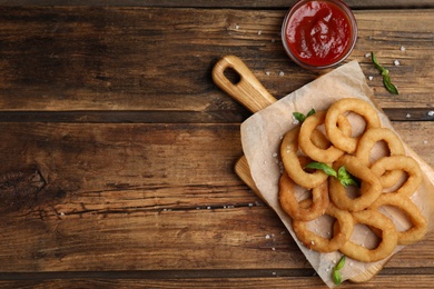 Delicious onion rings and ketchup on wooden table, flat lay. Space for text