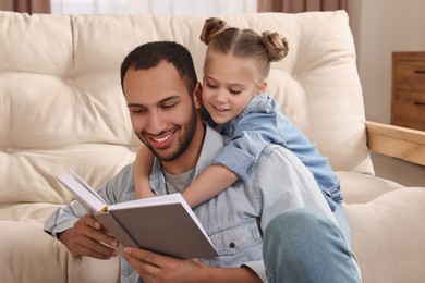 Photo of Little girl with her father reading book at home. International family