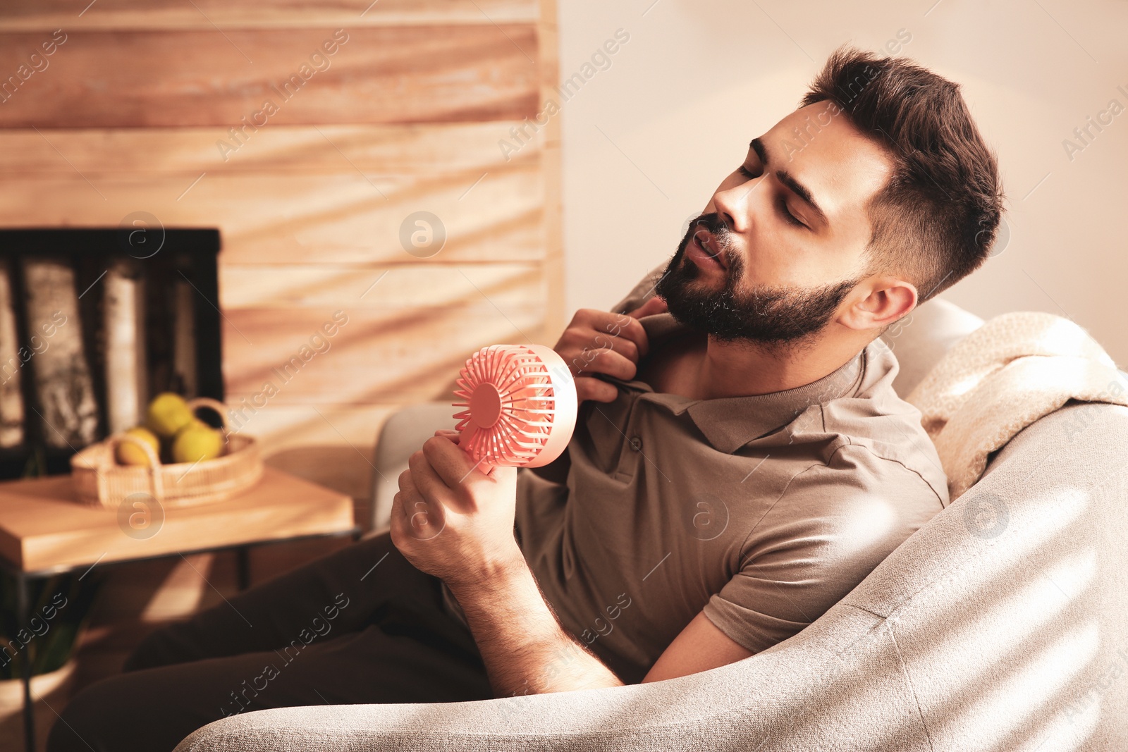 Photo of Man enjoying air flow from portable fan at home. Summer heat