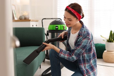 Photo of Young woman vacuuming sofa in living room