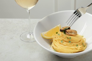 Photo of Eating tasty capellini with mussels and lemon from plate at light grey table, closeup. Exquisite presentation of pasta dish