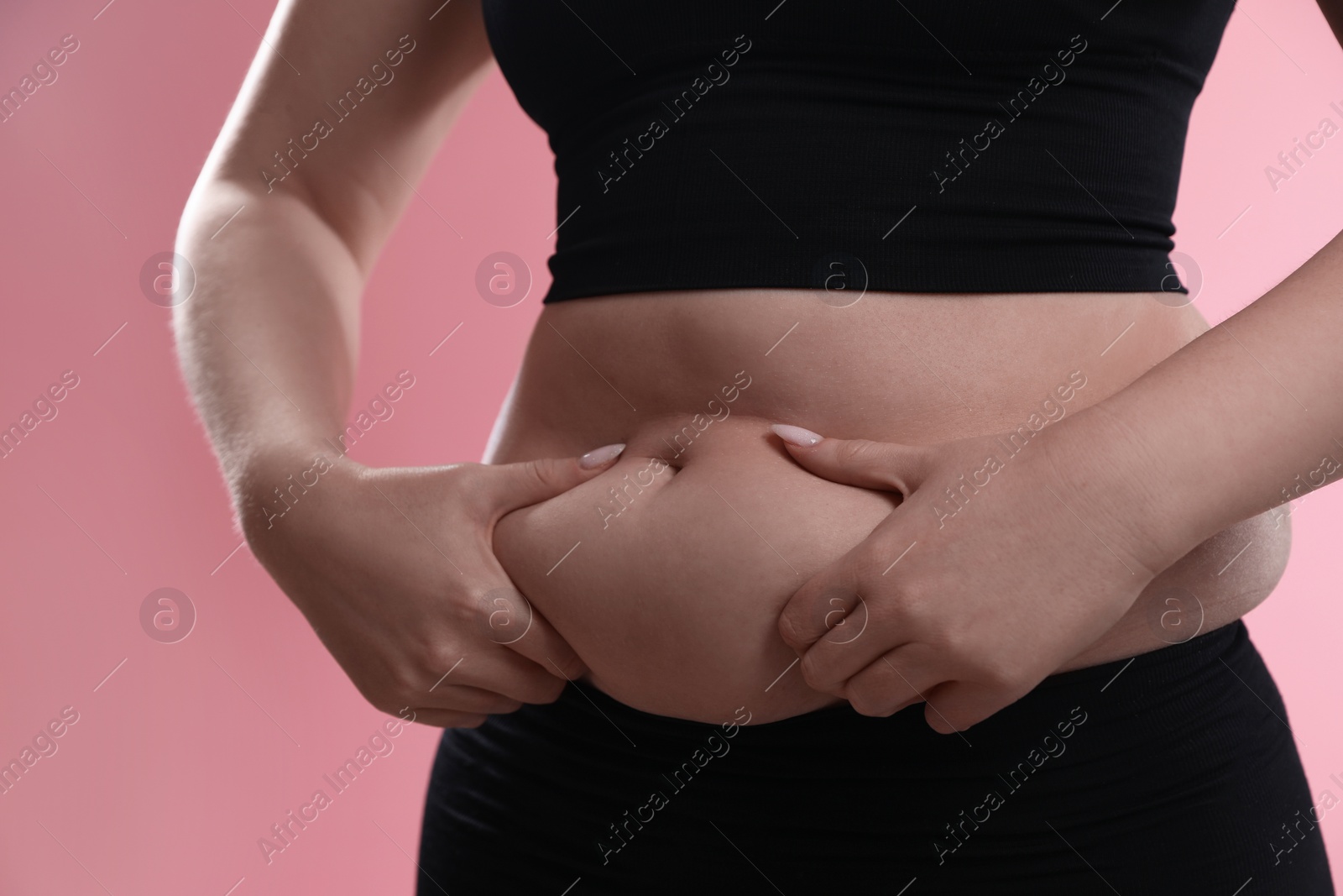 Photo of Woman touching belly fat on pink background, closeup. Overweight problem