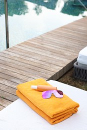 Photo of Beach towels, sunglasses and sunscreen on sun lounger near outdoor swimming pool, space for text. Luxury resort