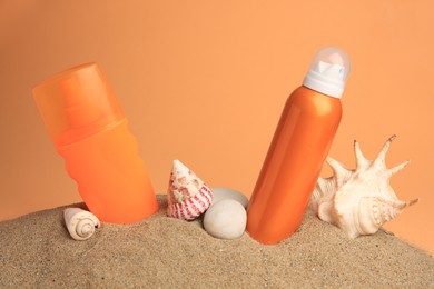 Photo of Sand with bottles of sunscreens, stones and seashells against orange background. Sun protection