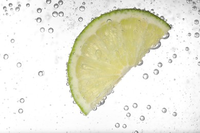 Photo of Juicy lime slice in soda water against white background, closeup