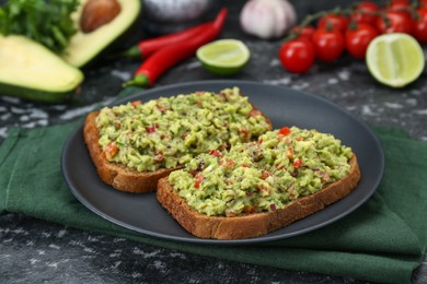 Slices of bread with tasty guacamole and ingredients on black textured table, closeup