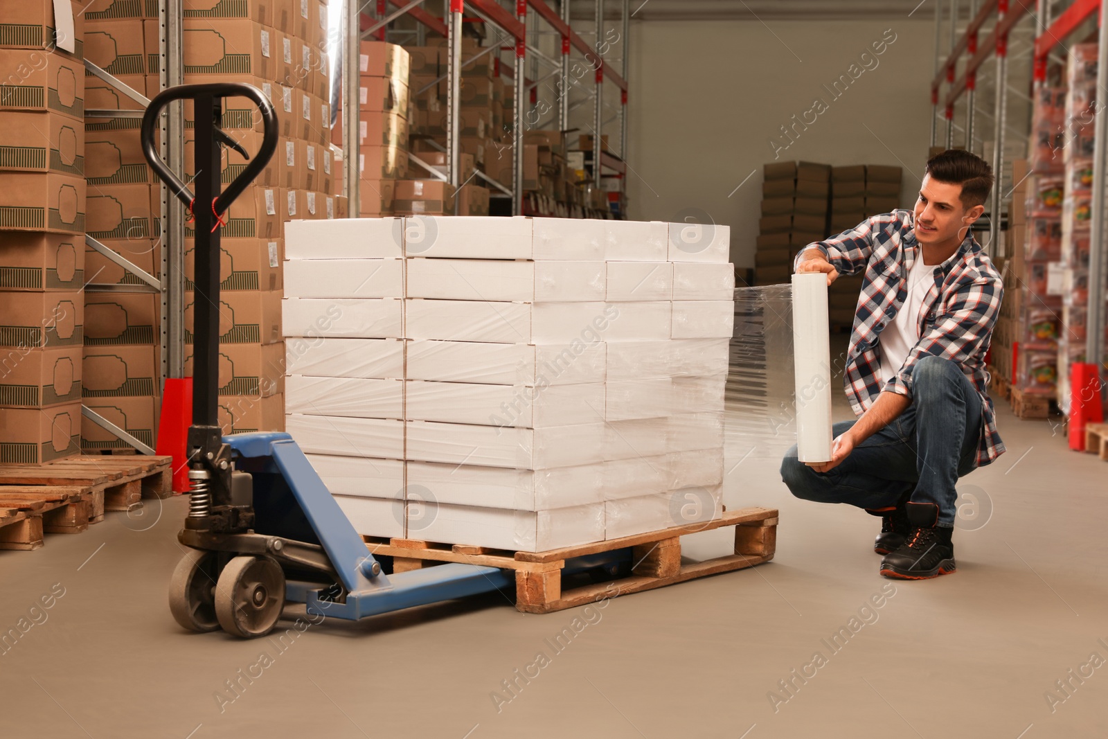 Photo of Worker wrapping boxes in stretch film at warehouse