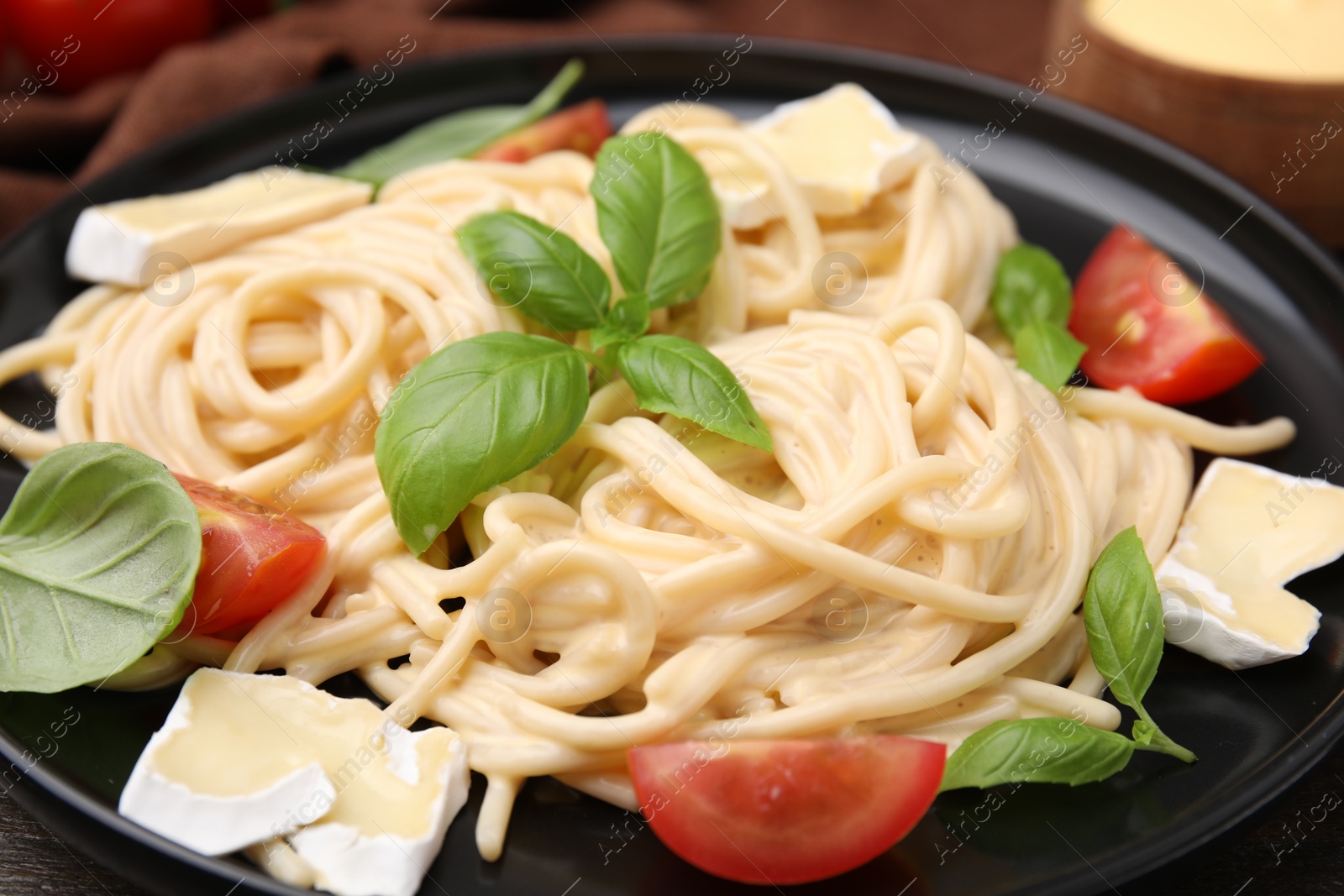 Photo of Delicious pasta with brie cheese, tomatoes and basil leaves on table, closeup