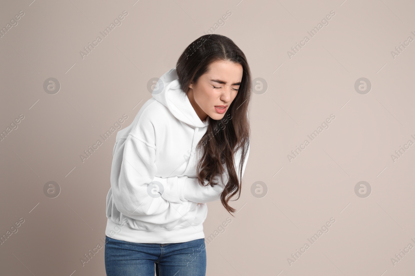 Photo of Young woman suffering from stomach ache on beige background. Food poisoning