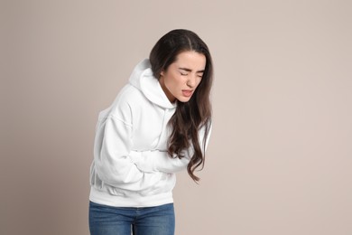 Photo of Young woman suffering from stomach ache on beige background. Food poisoning