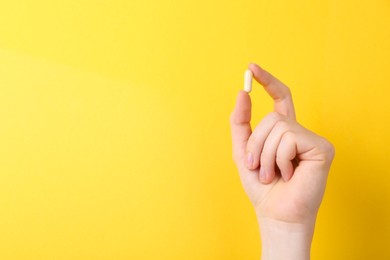 Woman holding vitamin capsule on yellow background, closeup. Space for text