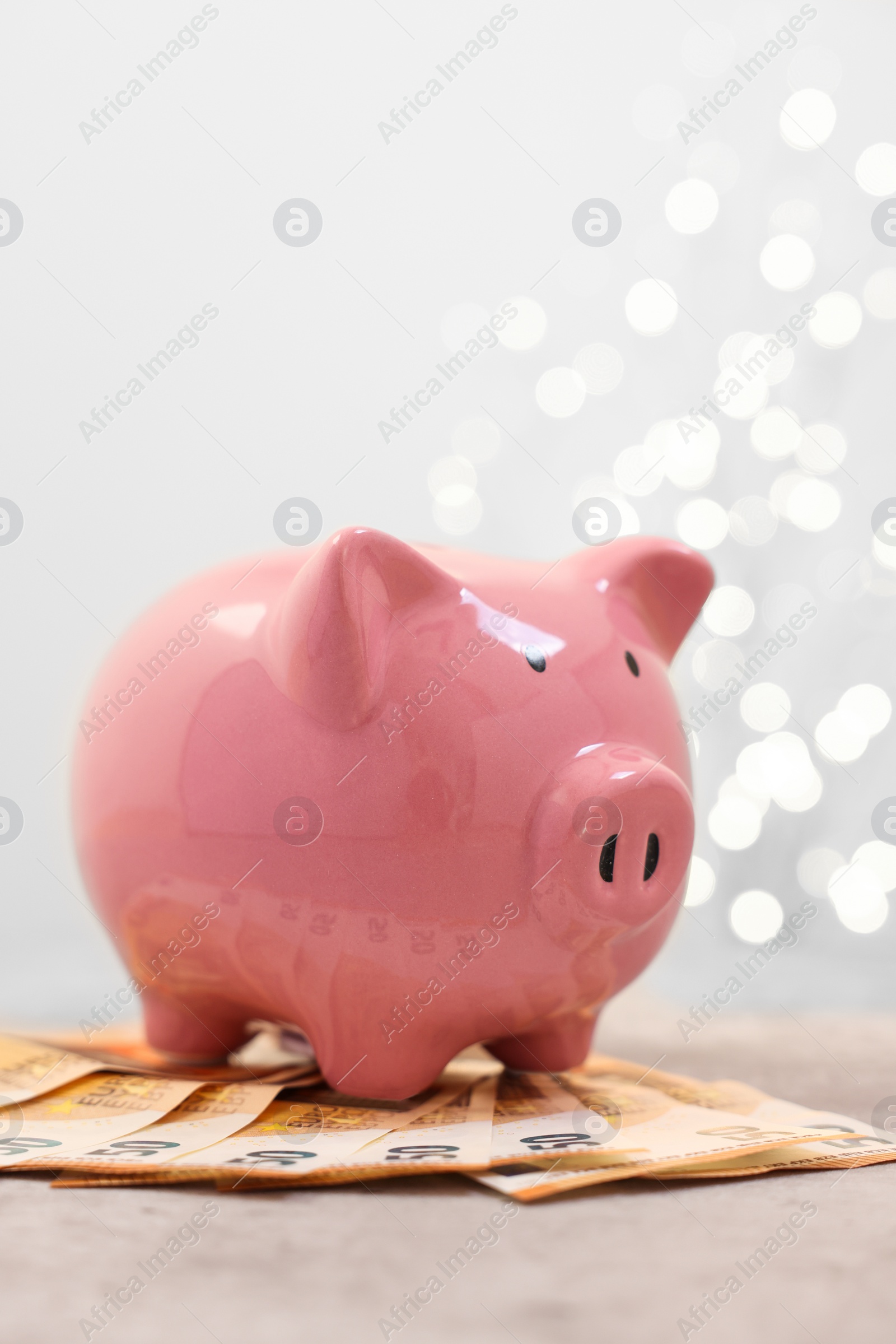 Photo of Piggy bank with euro banknotes on grey table against blurred lights