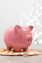 Photo of Piggy bank with euro banknotes on grey table against blurred lights