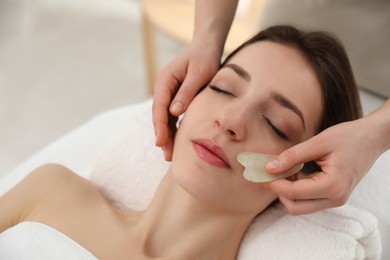 Young woman receiving facial massage with gua sha tool in beauty salon