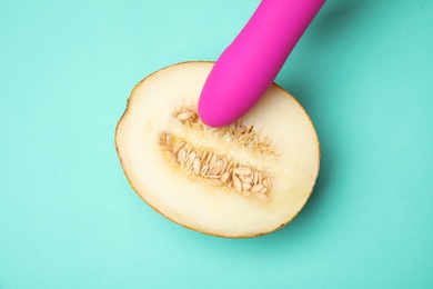 Photo of Half of melon and purple vibrator on turquoise background, flat lay. Sex concept
