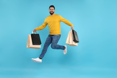 Happy man with many paper shopping bags jumping on light blue background