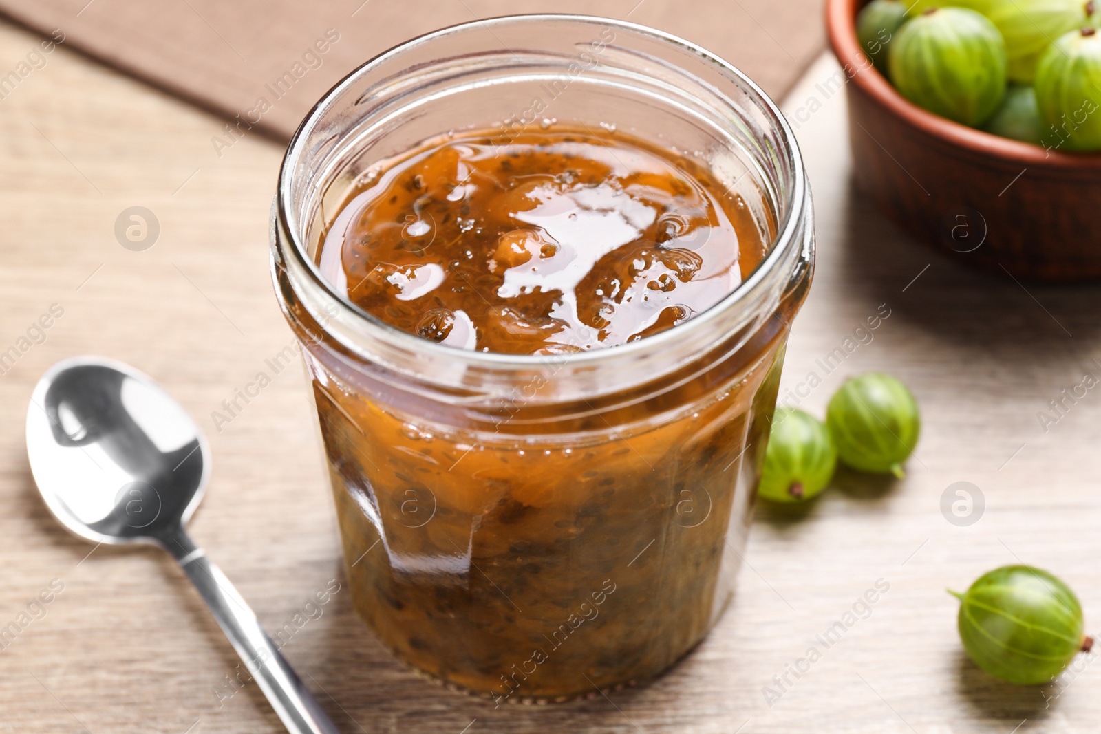 Photo of Jar of delicious gooseberry jam and fresh berries on wooden table, closeup