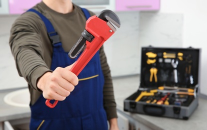 Photo of Male plumber holding pipe wrench in kitchen, closeup with space for text. Repair service