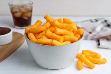 Photo of Crunchy cheesy corn snack in bowl, ketchup and refreshing drink on white wooden table, closeup