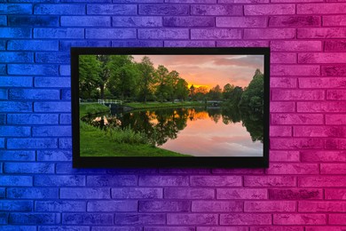 TV screen with beautiful landscape on brick wall in neon lights