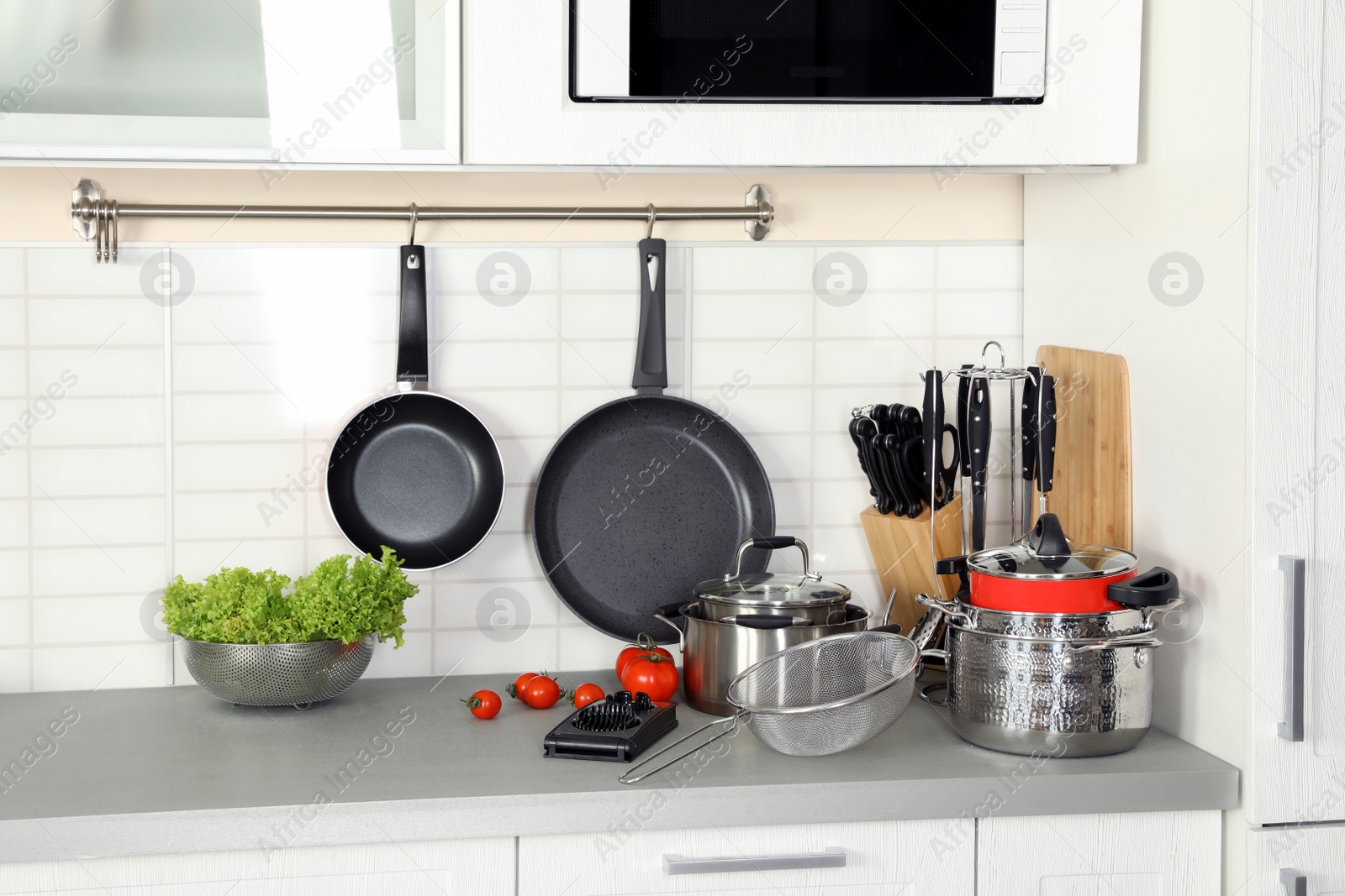 Photo of Set of clean cookware, utensils and products on table in modern kitchen