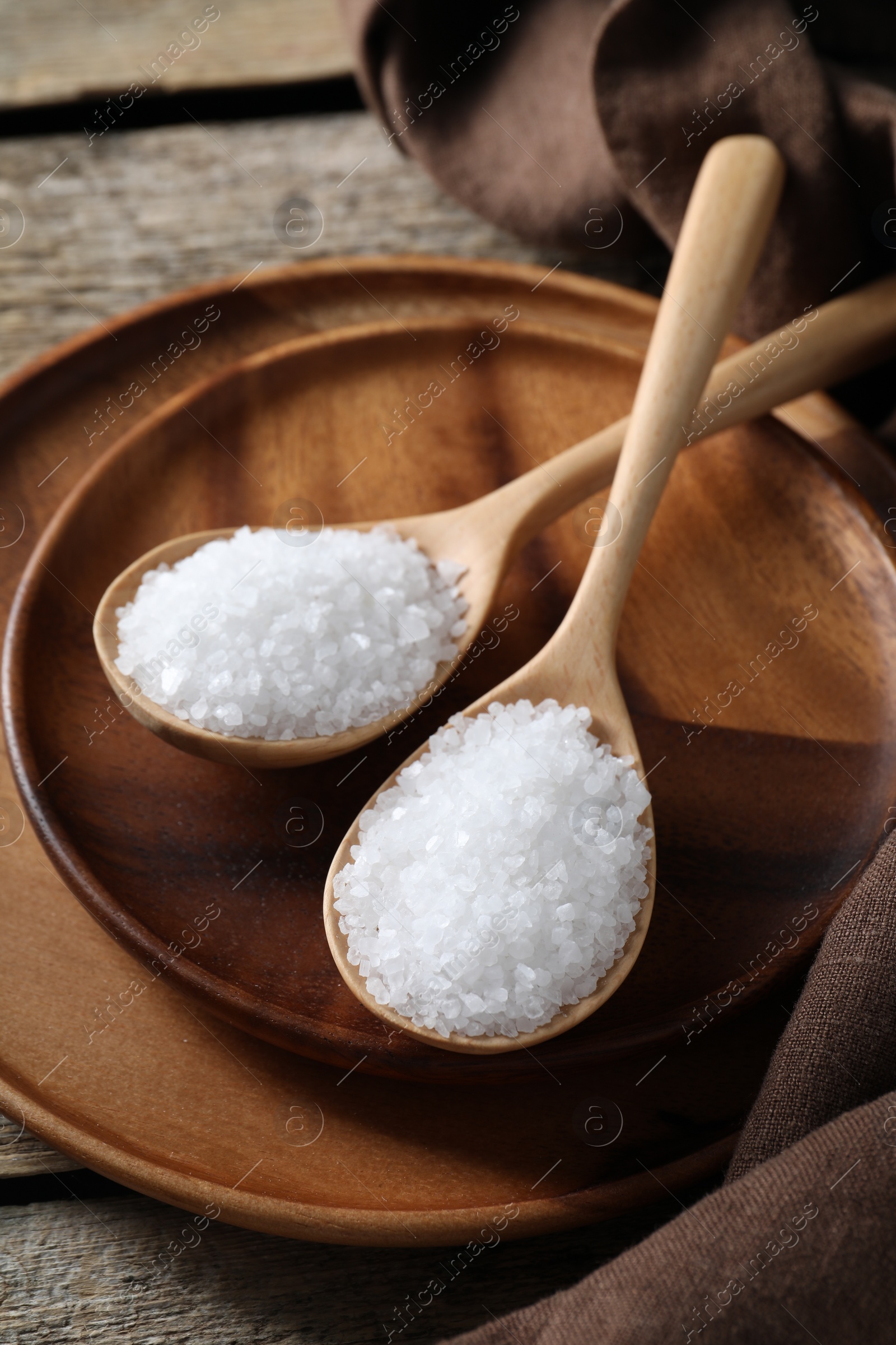 Photo of Organic salt in spoons on wooden table, closeup