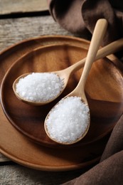 Photo of Organic salt in spoons on wooden table, closeup