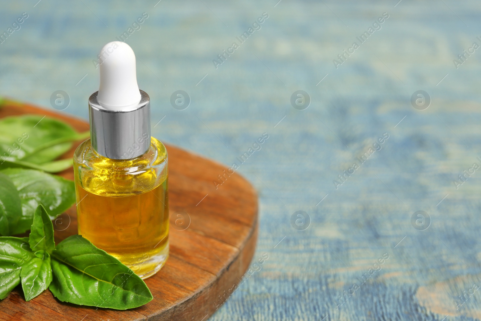 Photo of Wooden board with glass bottle of oil and basil leaves on table. Space for text